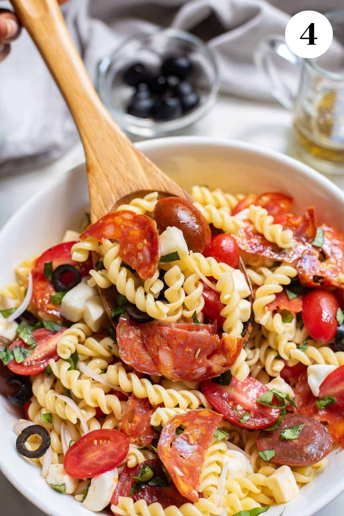 A bowl of pizza pasta salad with a spoon dipping out a serving.