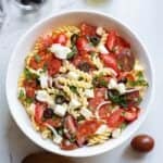 A white bowl filled with pizza pasta salad on the table with an olive next to the bowl.