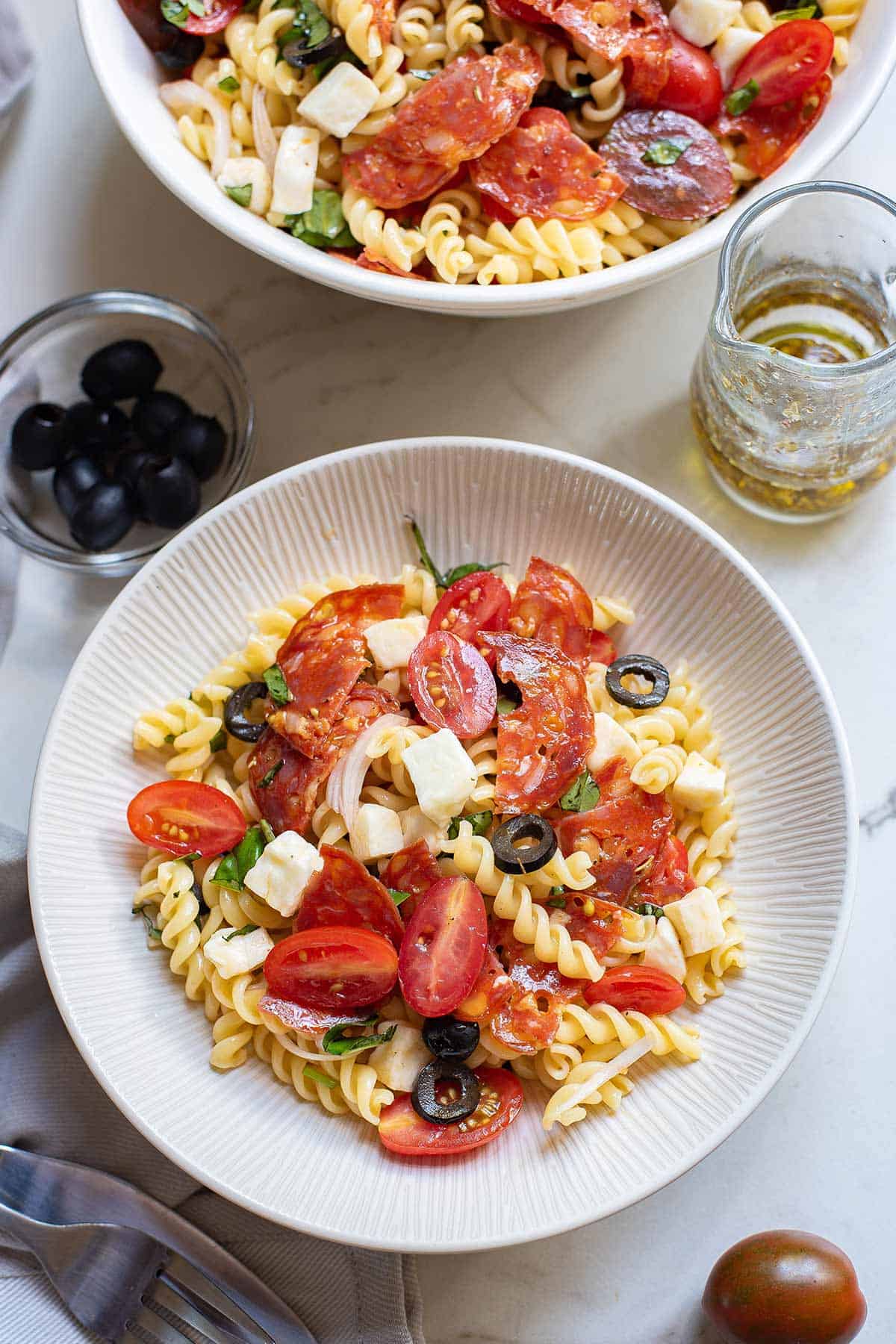 A plate of pizza pasta salad on the table with the bowl above it on the table.