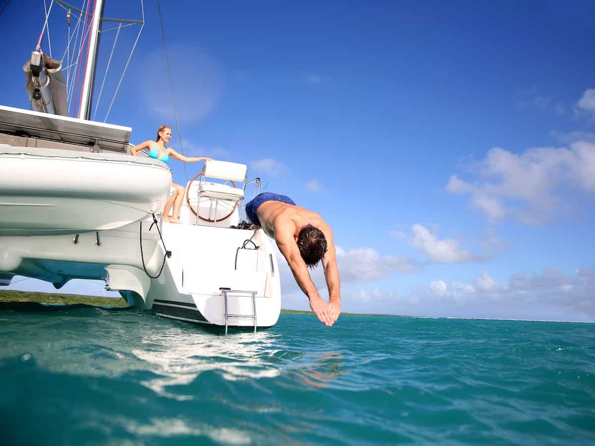 A man diving into the water from a catamaran. 