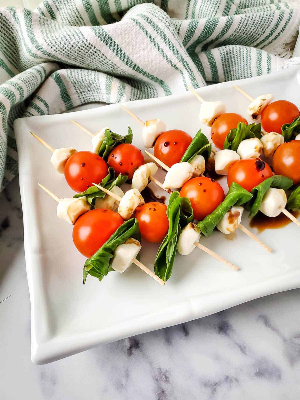 Tomato, mozzarella, and basil skewers on a white serving platter.