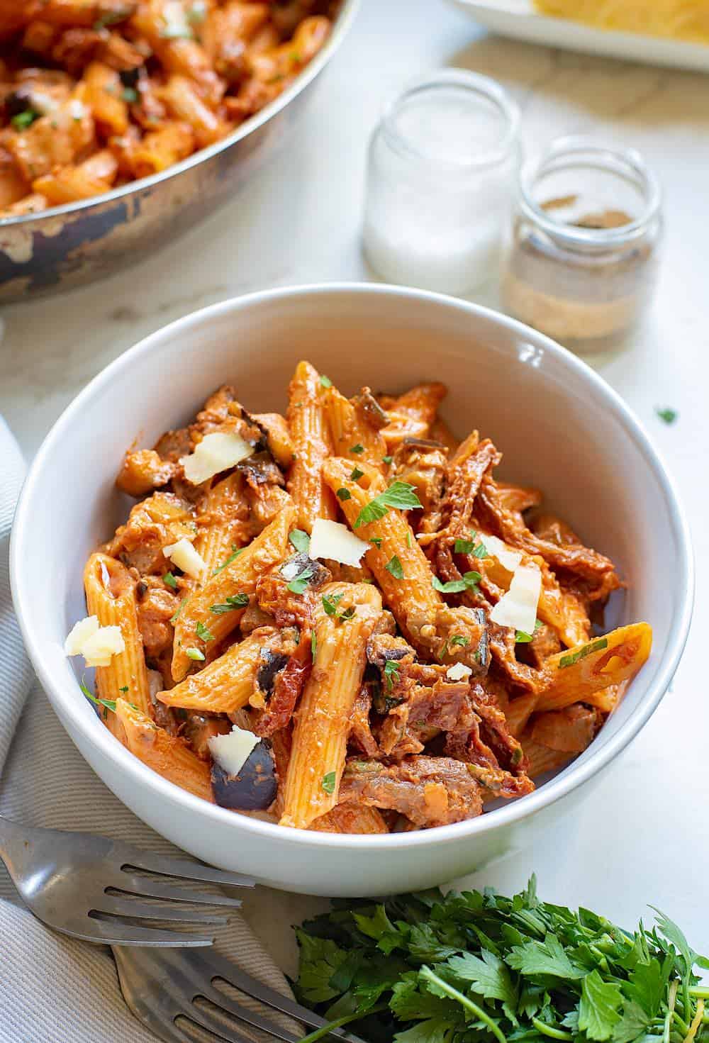A bowl of pasta with eggplant and sundried tomatoes on the table.