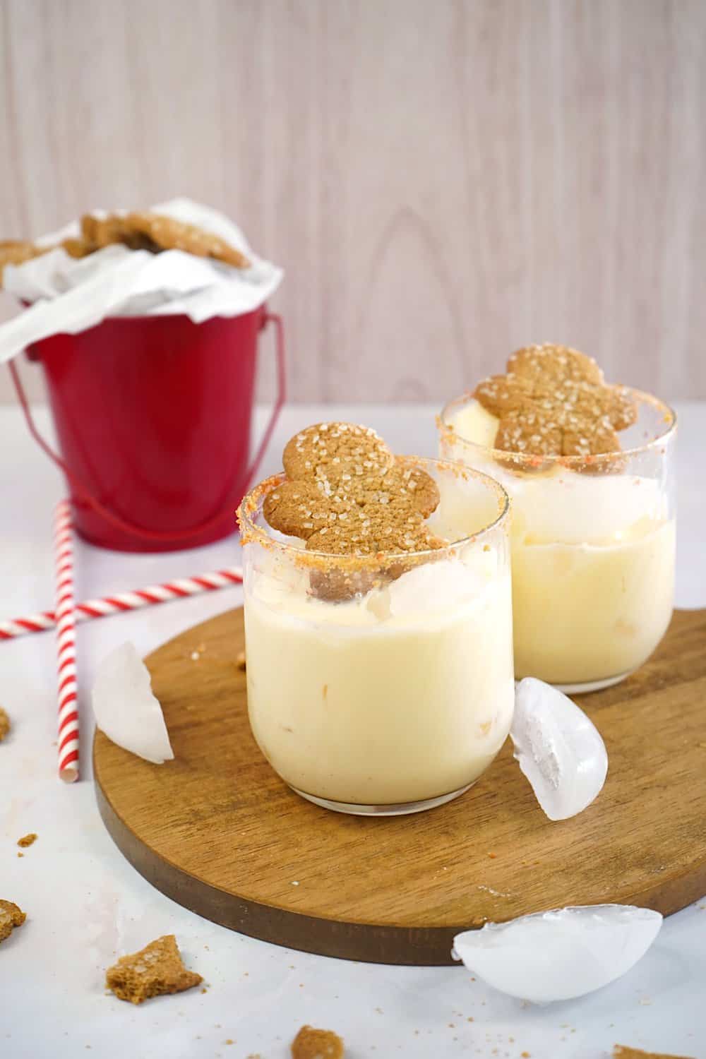 Eggnog cocktails with rum on the table with a bucket in the back and some straws.