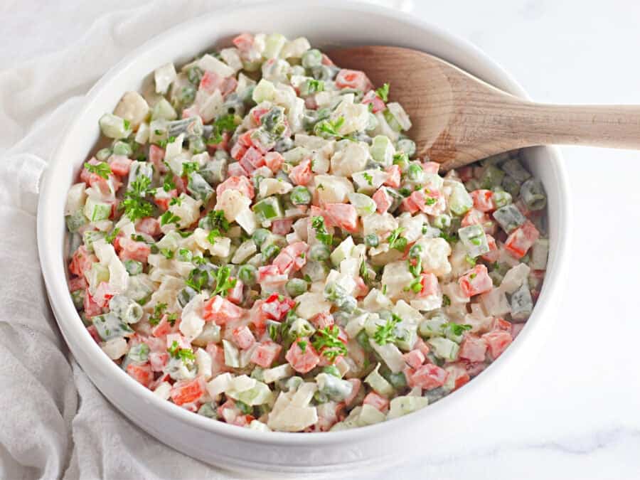 Guatemalan russian salad in a bowl with a wooden spoon.