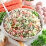 A bowl of Guatemalan russian salad on the table with fresh vegetables around it.