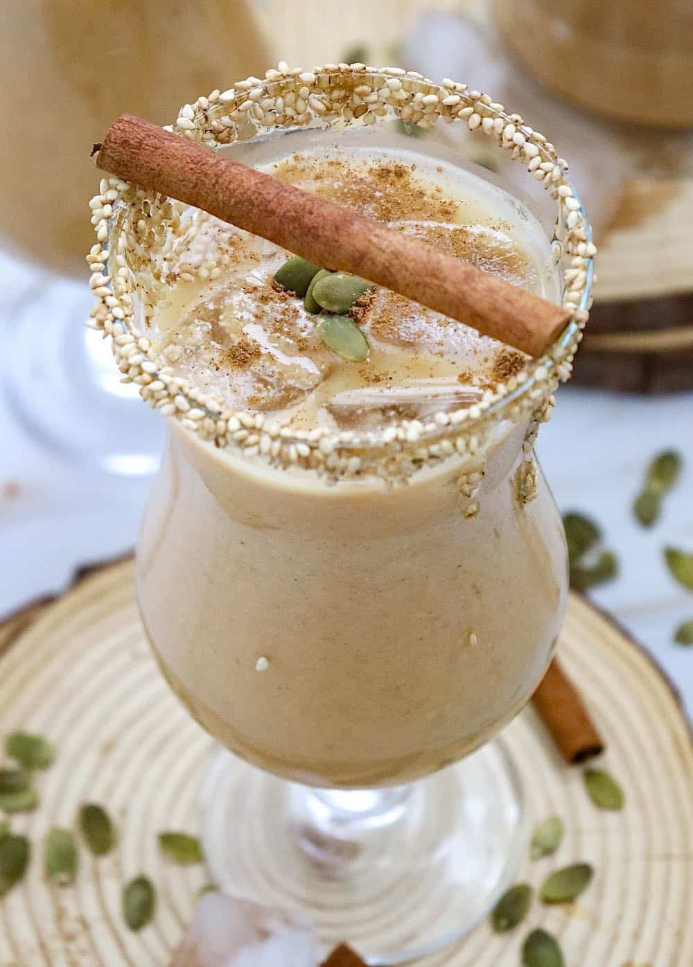Portrait of a tall glass of pumpkin spice horchata with sesame seed rim and pumpkin seeds.