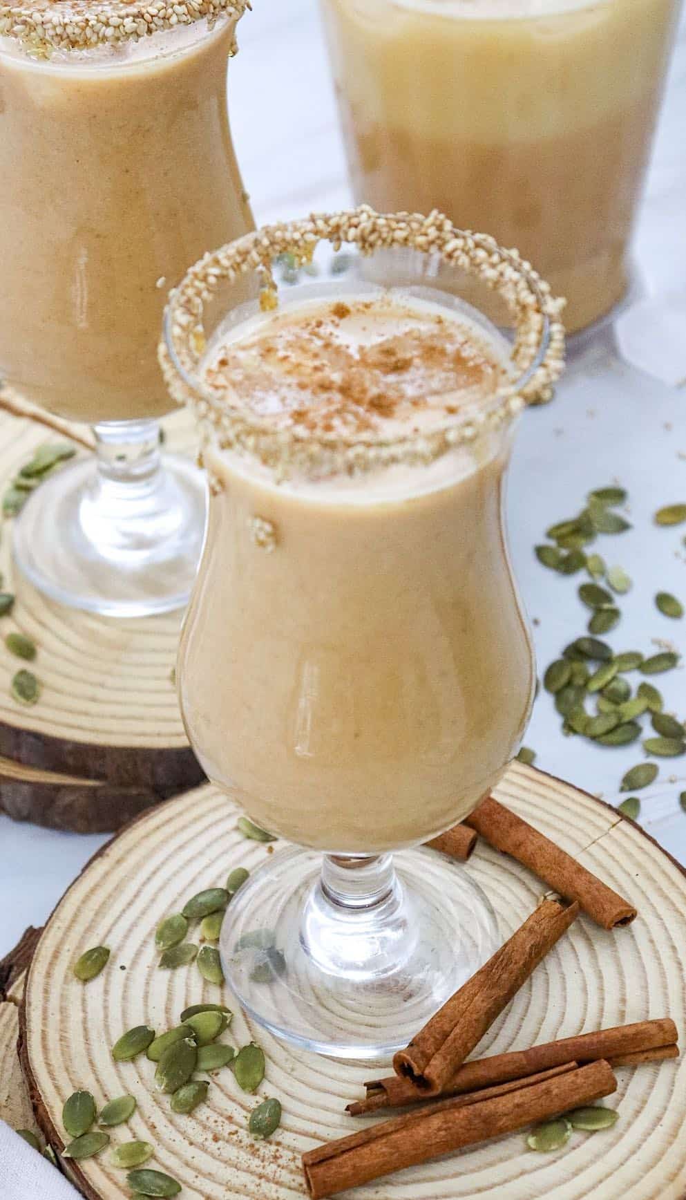 Two glasses of pumpkin pie spice horchata ( rice drink) with a pitcher in the background.