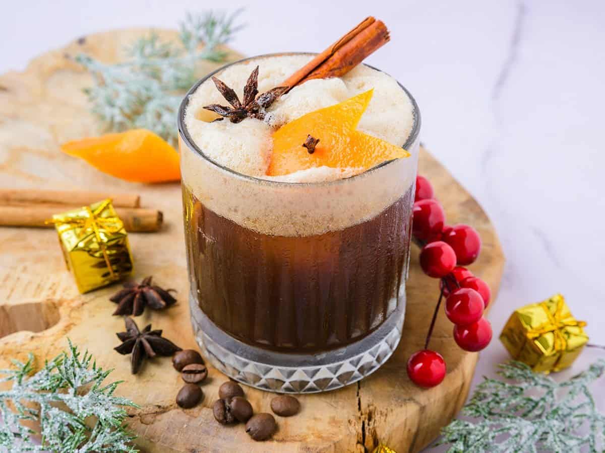 A glass of Christmas carajillo cocktail on the table garnished with cinnamon stick, star anise, and orange zest.