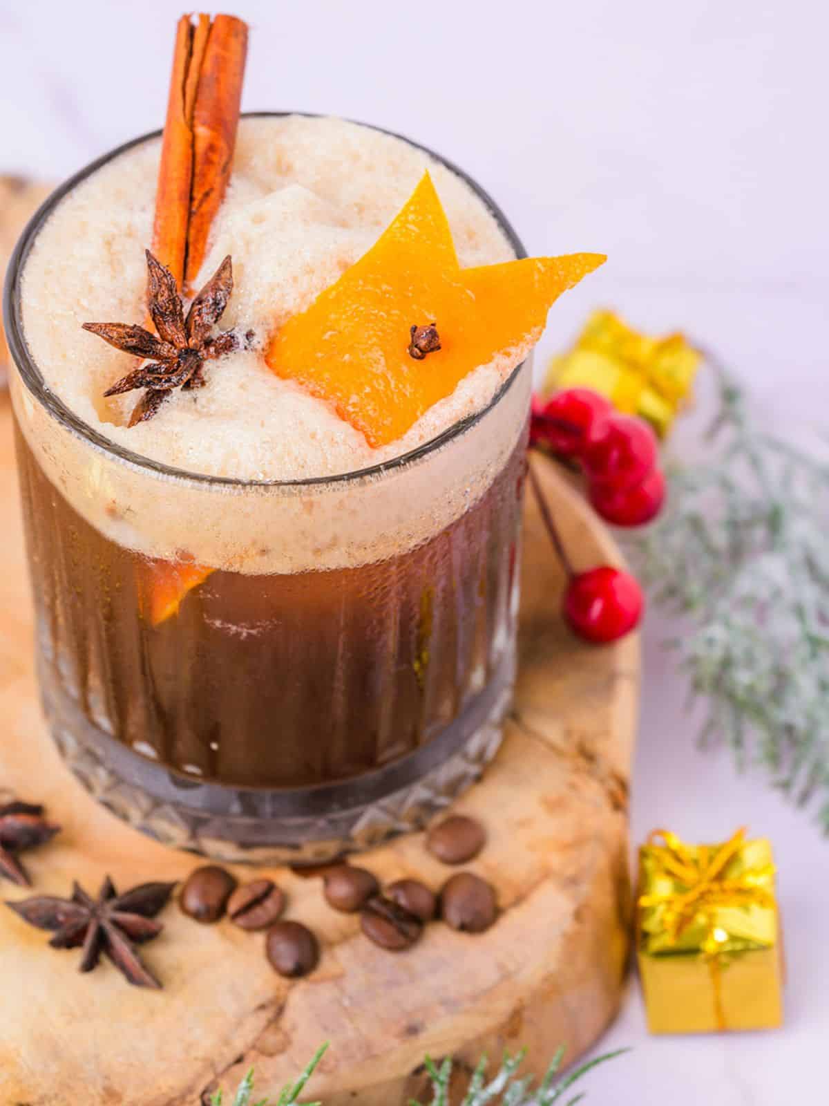 A carajillo drink garnished with orange peel, star anise and cinnamon stick.