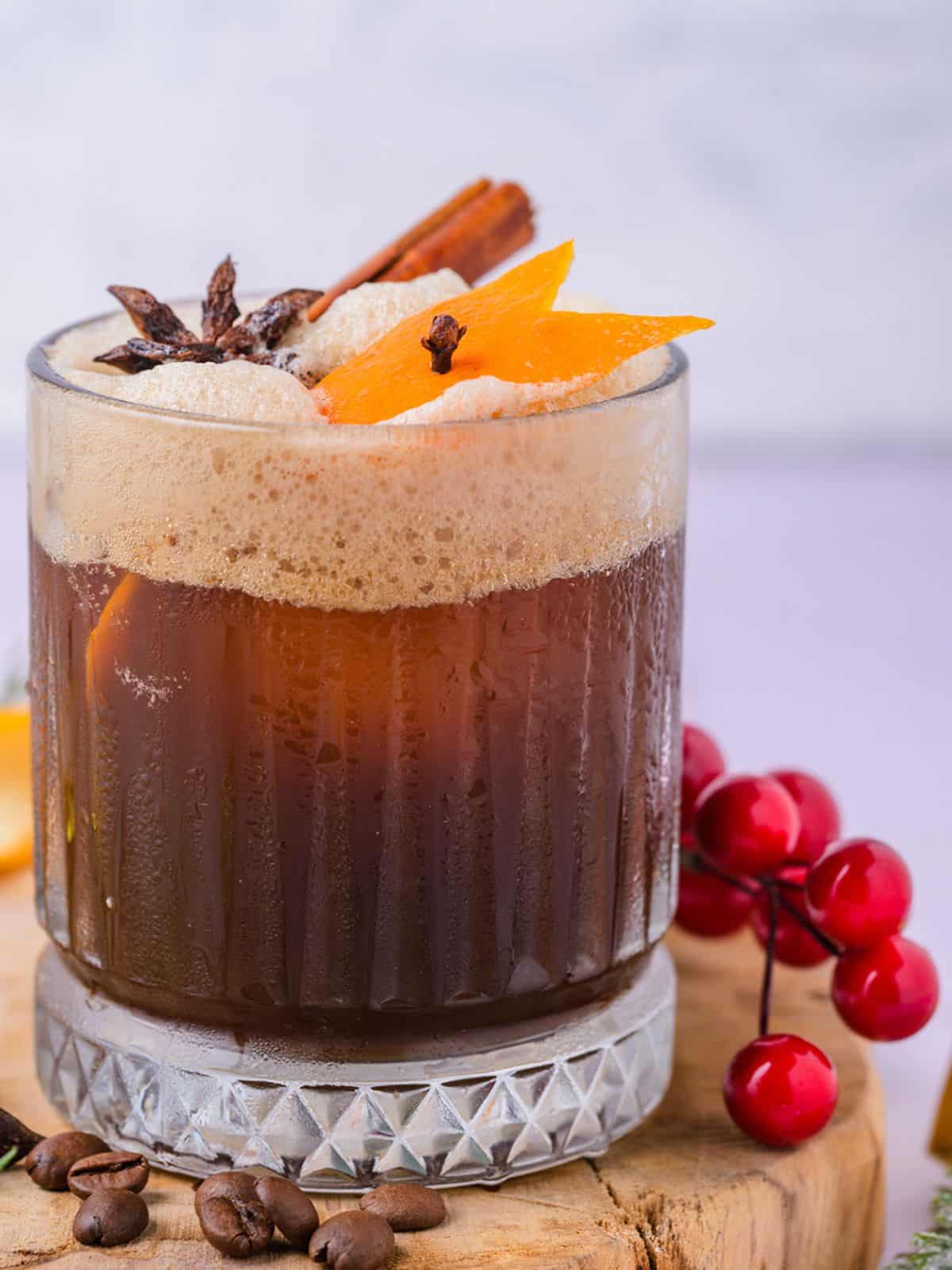 A glass of Christmas carajillo drink on a wooden block with cranberries around it.