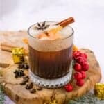 A Christmas carajillo cocktail on a wooden block with cranberries and coffee beans scattered around it.