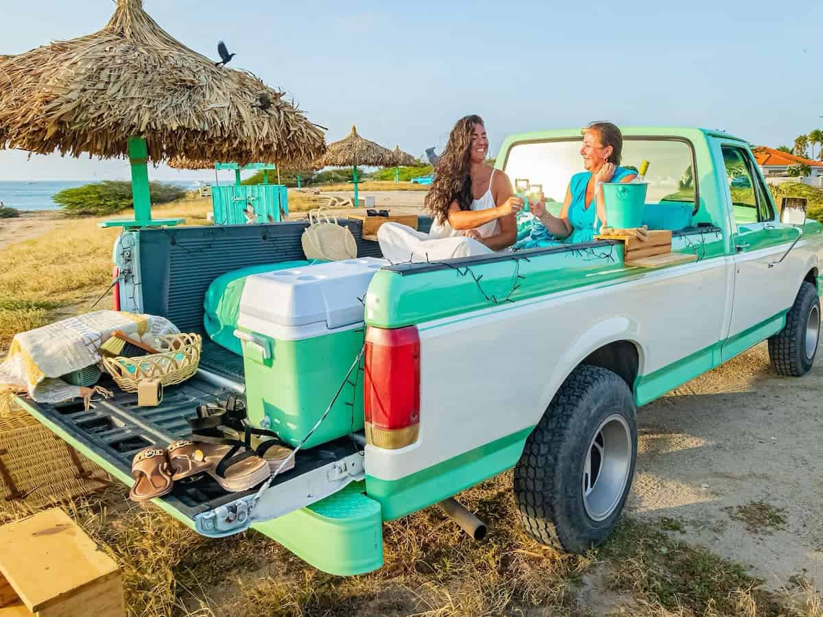 Two people in a pick up truck on a beach in Aruba. 
